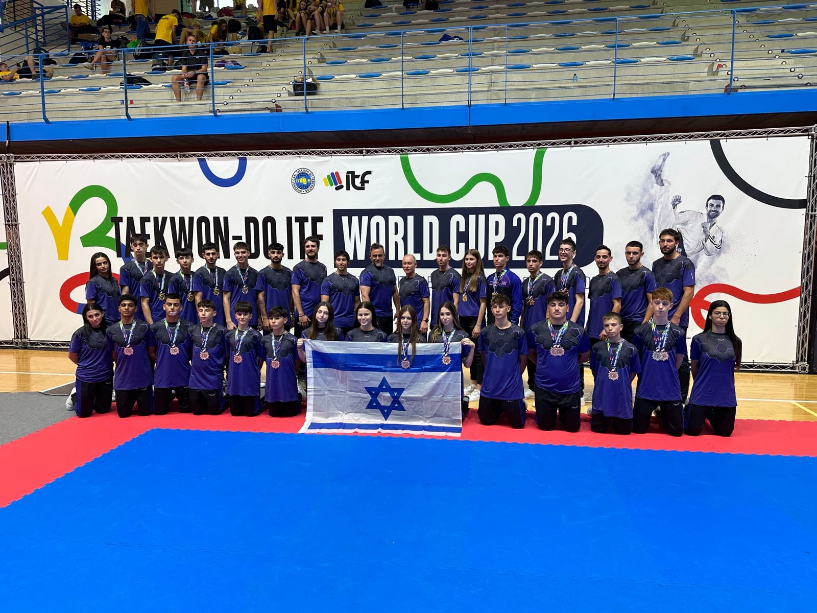 נבחרת Legacy Team עם המדליות ודגל ישראל, מול שלט גביע העולם 2026